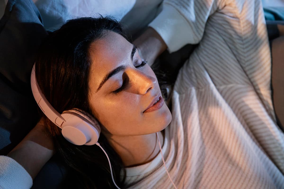 Woman lying down with pink headphones and eyes closed