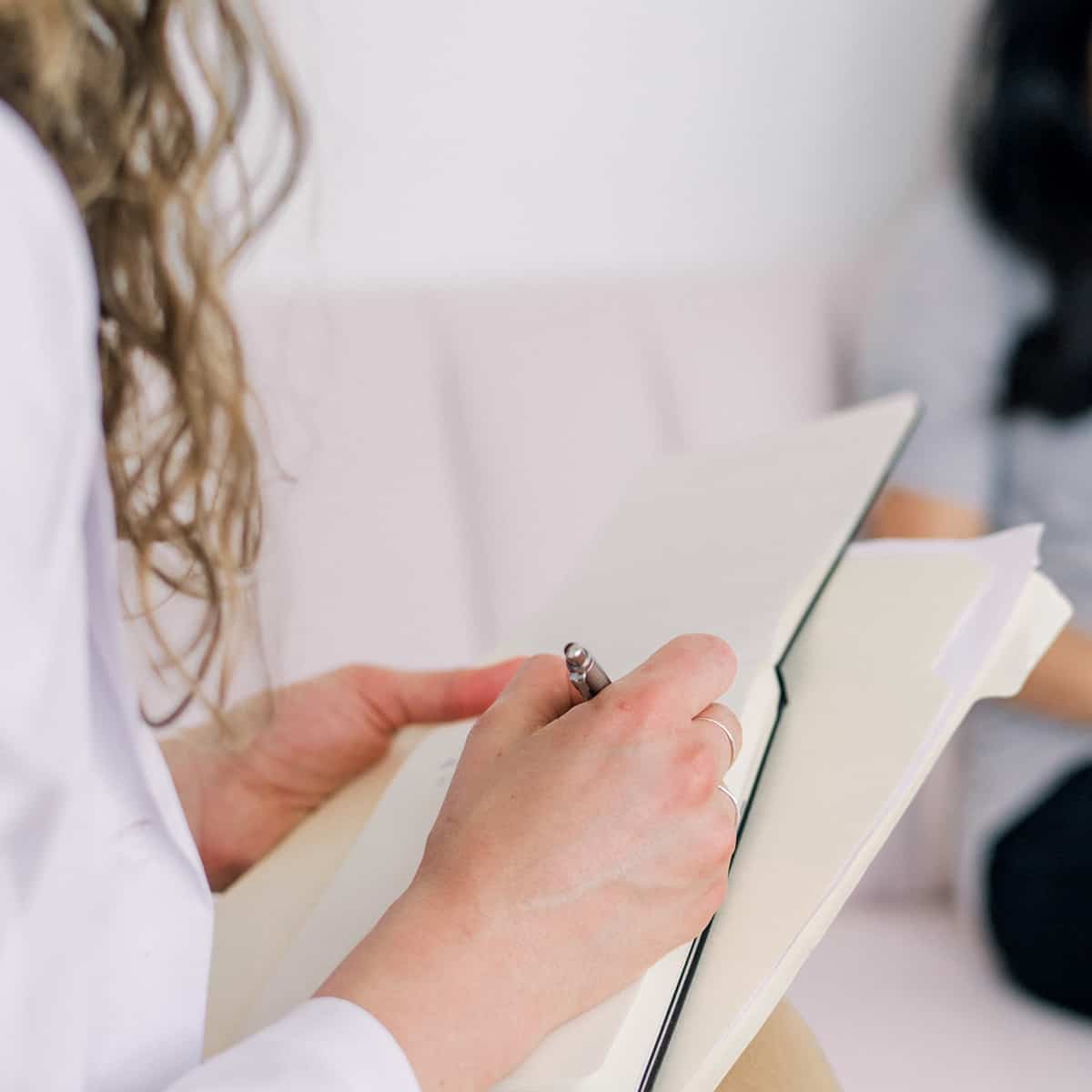 A woman on a couch, engaged in writing notes in a notebook with a pen, surrounded by a cozy living room.