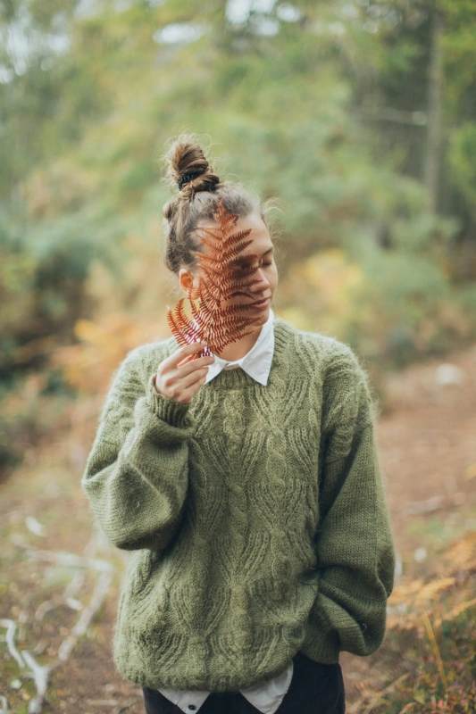 A woman in a green sweater holds a vibrant leaf, showcasing her connection to nature.
