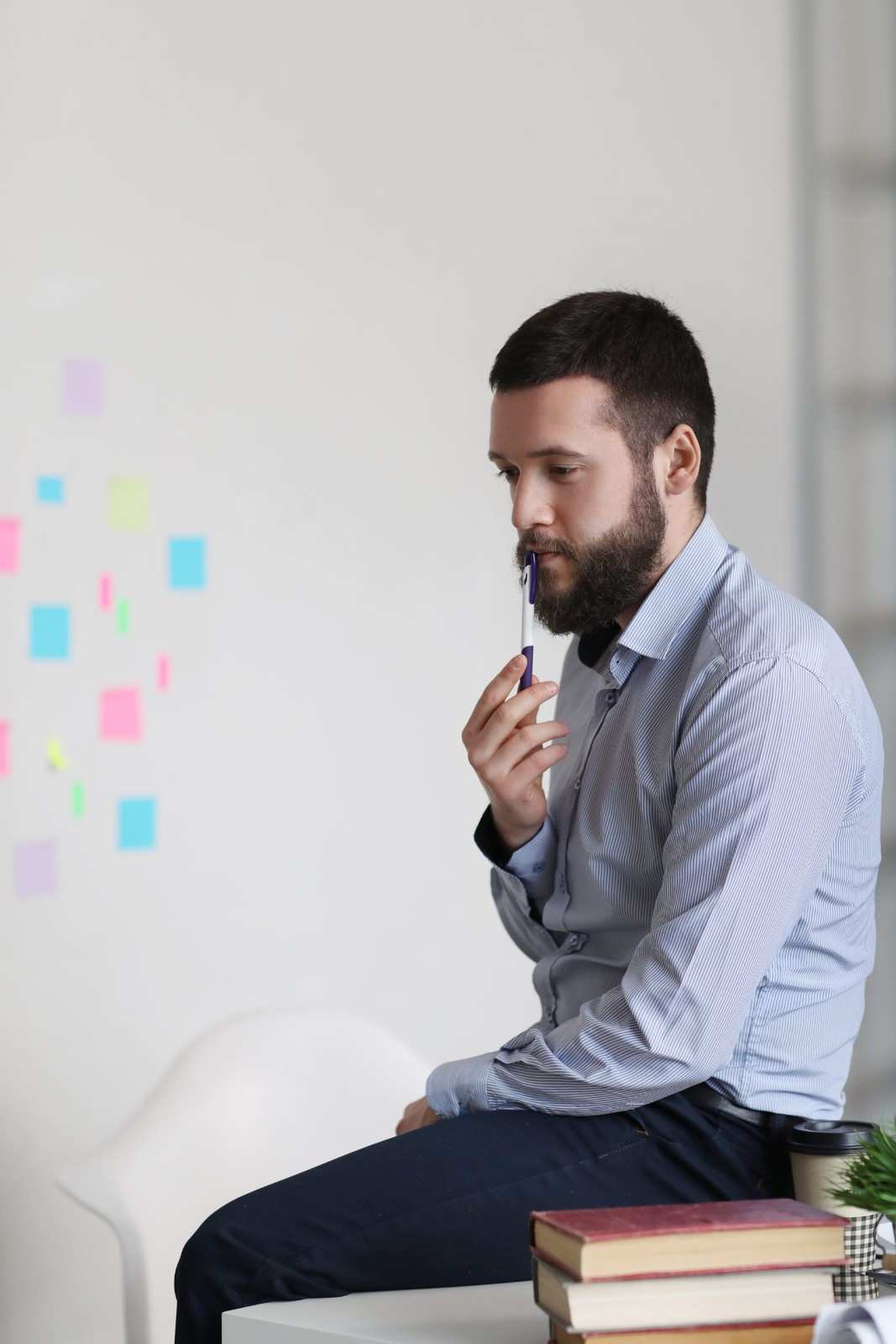 A man sits on a chair with a pen in his mouth, appearing deep in thought or contemplation.