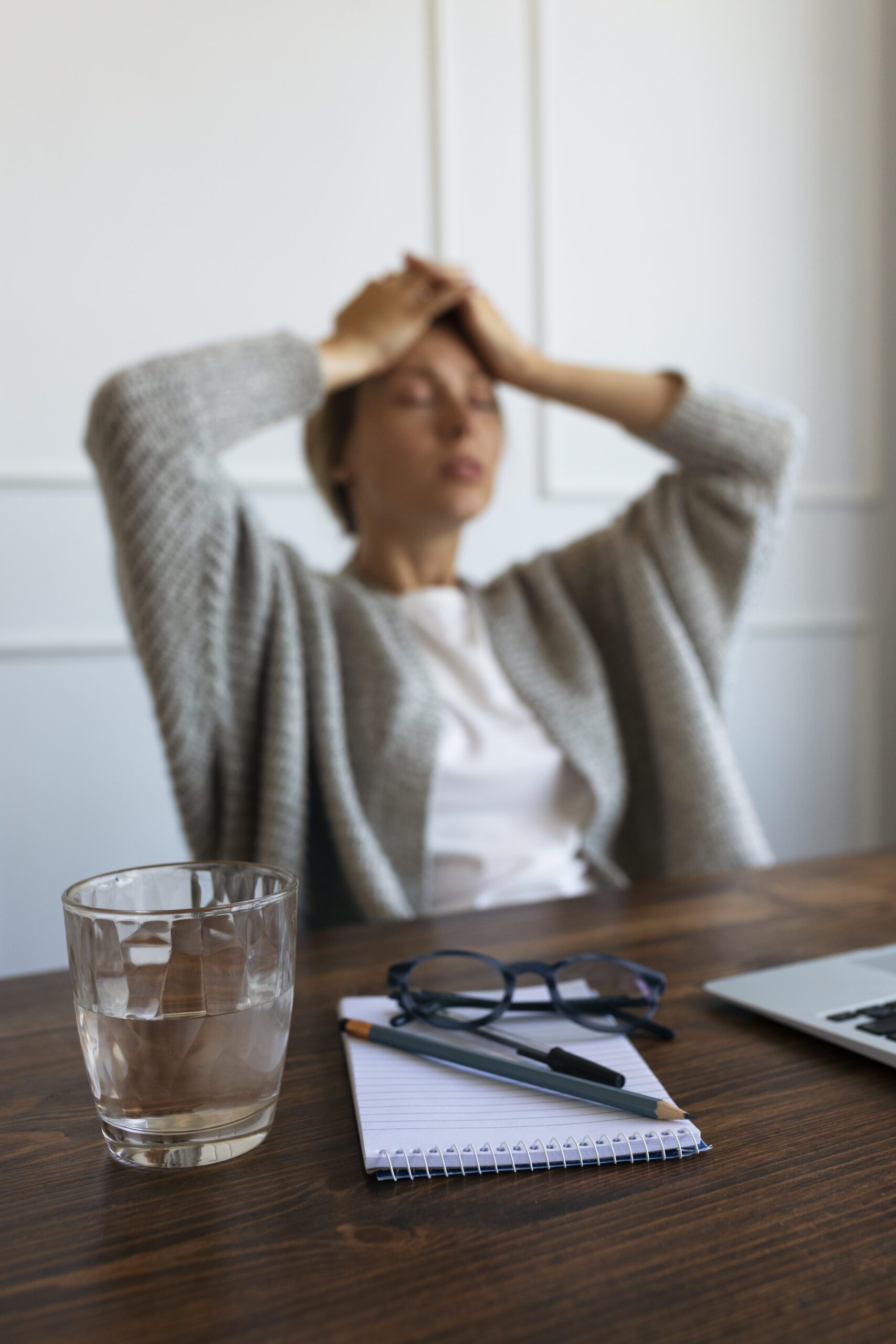 A woman sitting at a desk, resting her head in her hands, appears deep in thought or stressed.