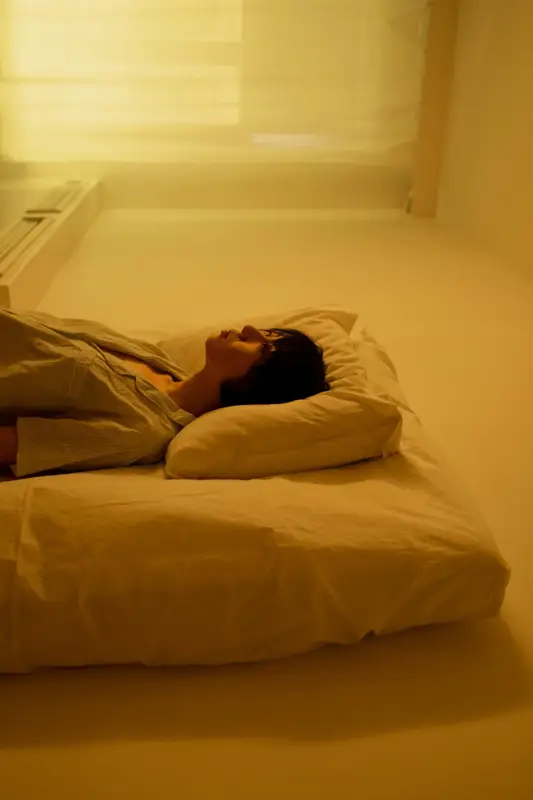A person lying on a bed in a cozy room, surrounded by soft lighting and simple decor.
