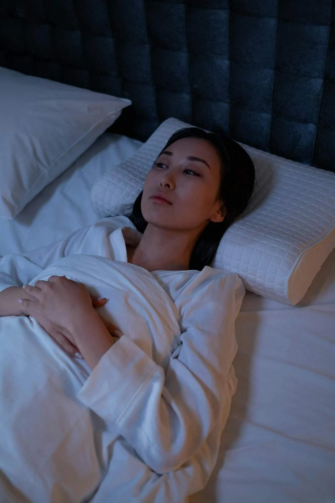 A woman lying in bed with her eyes closed, appearing relaxed and peaceful.