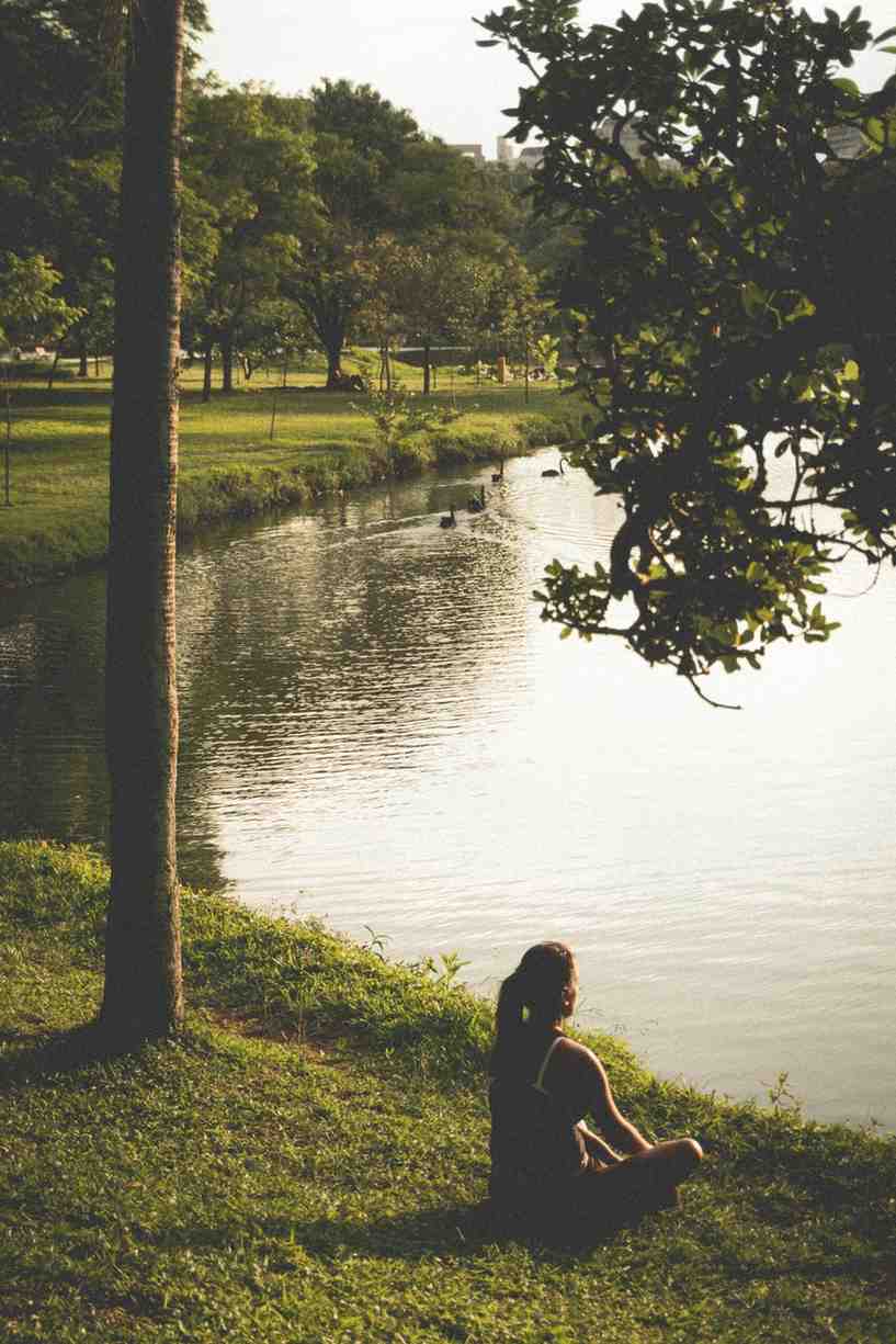A woman sitting on the grass by a serene lake, enjoying the peaceful natural surroundings.