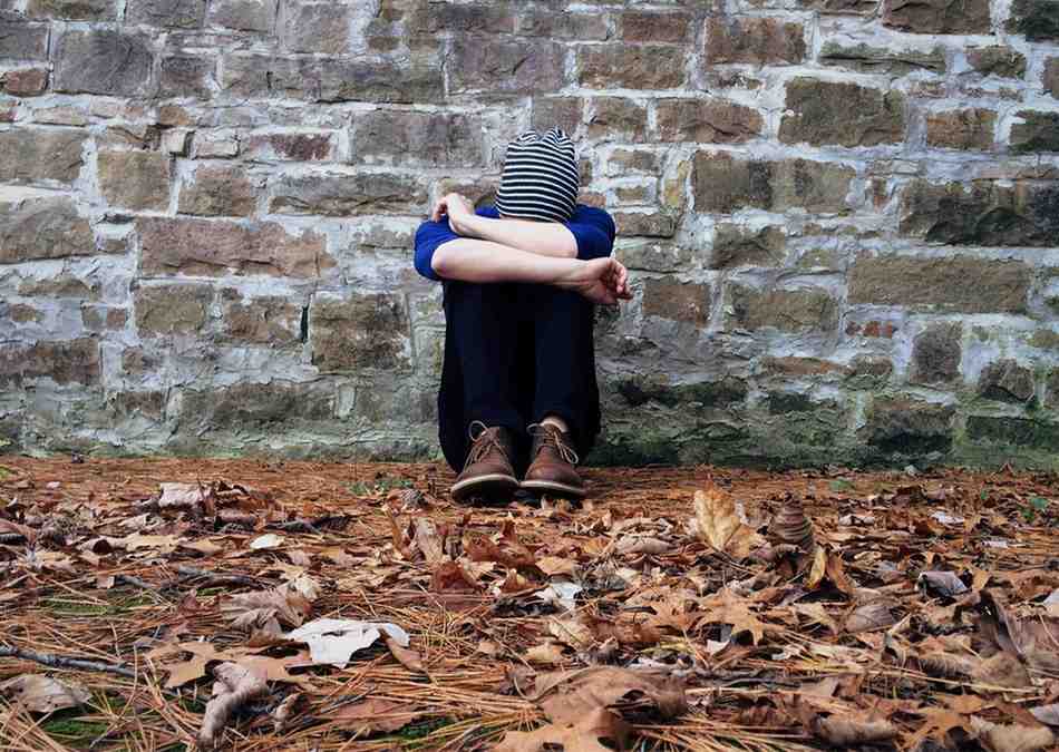 A person sitting on the ground with their hands covering their face, conveying a sense of distress or contemplation.
